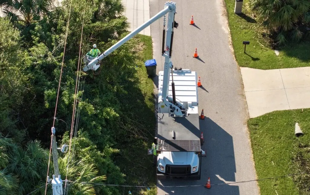 A high-angle perspective shows professional utility workers performing maintenance on electrical lines from a white bucket truck.